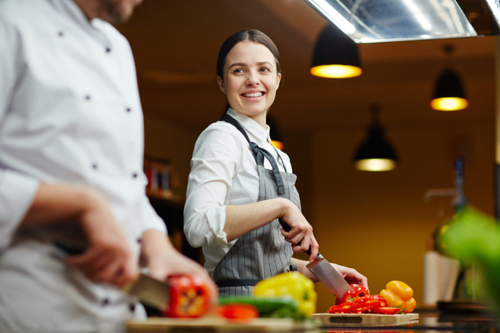 Smiling trainee talking to expert while cutting raw pepper